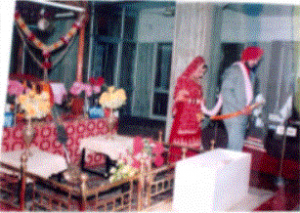 ピンクの帯状のもので二人をつないでいる。二人でグルの前に進み、結婚を認めてもらう。